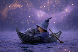 newborn baby in witch costume on wooden boat under night sky with halloween elements