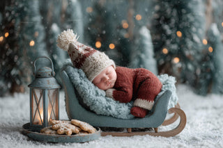 newborn baby in winter wonderland scene with christmas backdrop and santa sleigh
